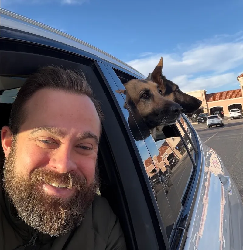 Philip smiling in the driver's seat while Shelby and another German Shepherd lean out the back window